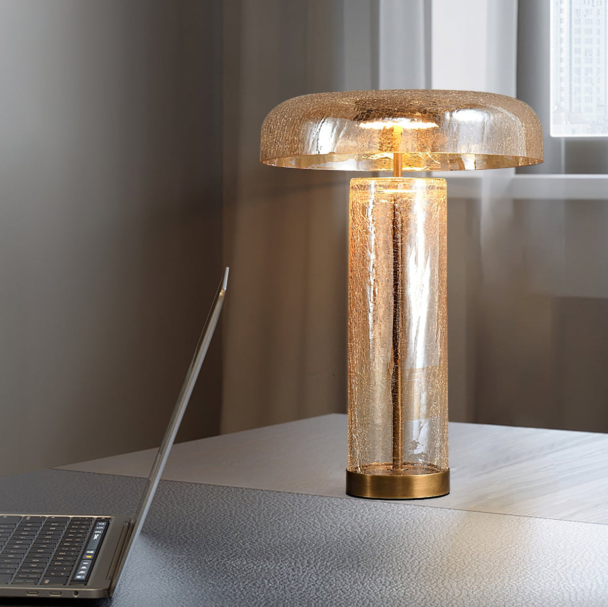 Lit Clérachic table lamp with an amber glass dome on a grey desk, a laptop at the left and a window behind.