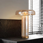 A Clérachic crackle-glass table lamp on a dark wood chest, the amber dome glowing above its see-through cylinder body.