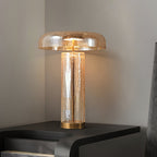 Clérachic table lamp with an amber crackle-glass dome and a bronze foot, lit on a dark nightstand against a grey wall.