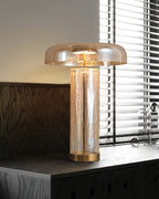 Lamp from Clérachic on a dark wood cabinet below a blind-covered window, the cracked glass body warm with light.