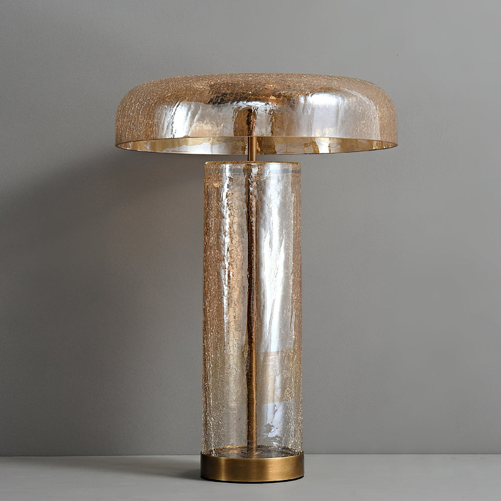 Front view of an unlit Clérachic table lamp against a grey wall, with a gold-lined dome over a crackle-glass cylinder.