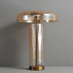 Front view of an unlit Clérachic table lamp against a grey wall, with a gold-lined dome over a crackle-glass cylinder.