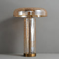 Clérachic crackle-glass table lamp switched off on a grey ledge, its amber dome and clear cylinder showing a fine crack pattern.