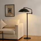 Clérachic black floor lamp lit beside a cream upholstered sofa, its dome dropping light over the seat.