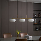 Clérachic gold-frame cream glass cluster hanging over a stone-grey dining table with brown leather chairs.
