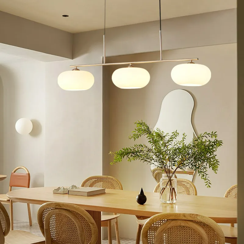 Clérachic cream glass 3-light cluster in gold over a pale wood table with cane-back chairs and a wavy mirror.