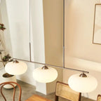 Clérachic gold-frame cream glass pendant over a wood dining table, two gold rods and a rattan chair behind.