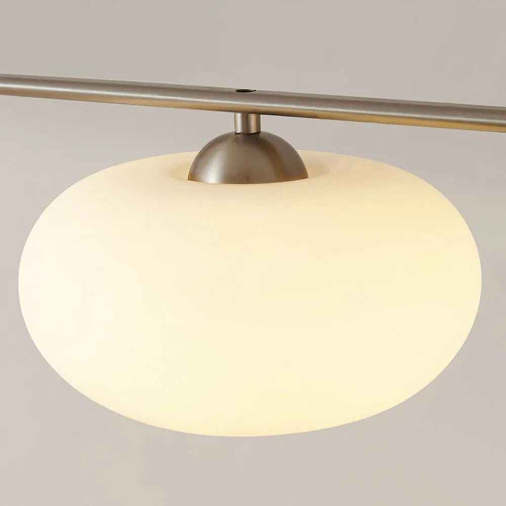 Close-up of a Clérachic cream glass shade on the gold-frame cluster, gold dome cap seated on the glowing globe.