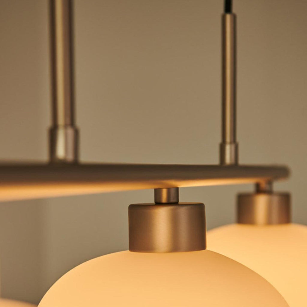 Close-up of the Clérachic gold bar and twin rods, cream glass shades glowing beneath two gold mounting caps.