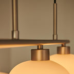 Close-up of the Clérachic gold bar and twin rods, cream glass shades glowing beneath two gold mounting caps.