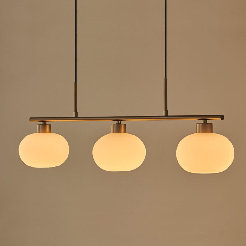 Clérachic cream glass 3-light cluster in gold, three lit oval shades on a gold bar against a warm beige ground.