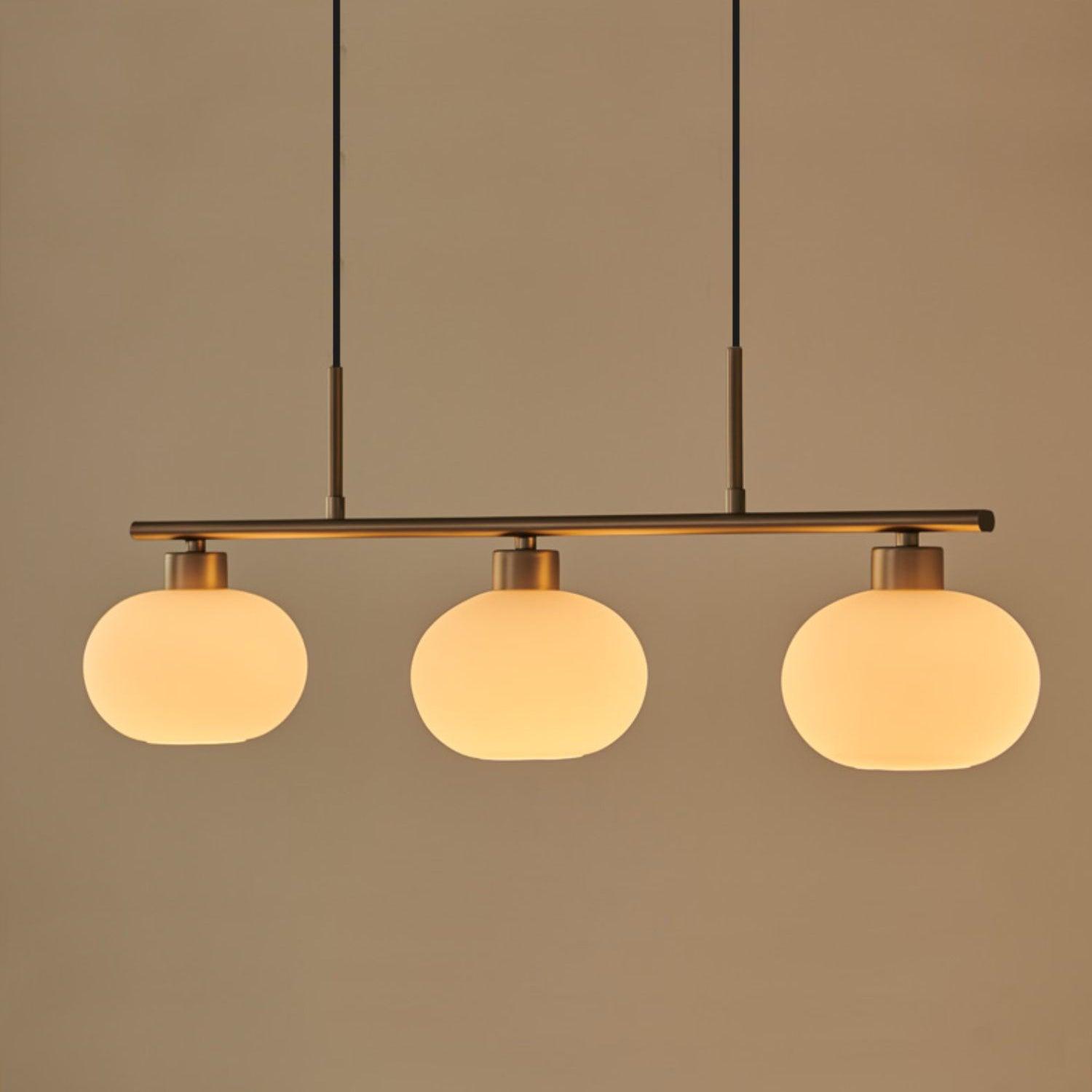 Clérachic cream glass 3-light cluster in gold, three lit oval shades on a gold bar against a warm beige ground.