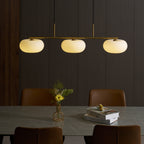 Clérachic gold-frame cream glass cluster lit over a marble dining table with leather chairs and stacked books.