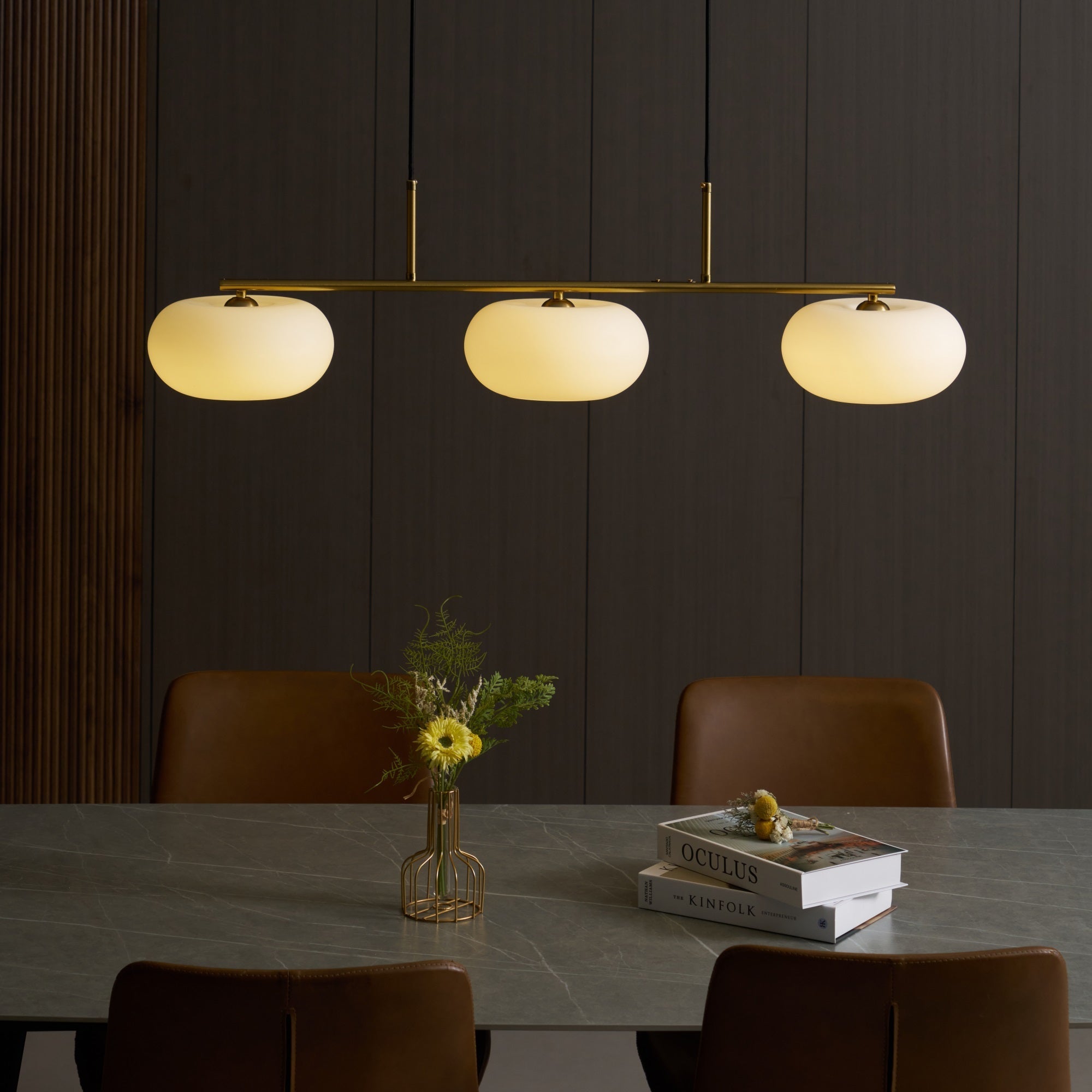 Clérachic gold-frame cream glass cluster lit over a marble dining table with leather chairs and stacked books.