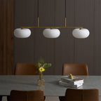 Unlit Clérachic gold-frame cream glass 3-light cluster over a marble table, dark wood panels and leather chairs.