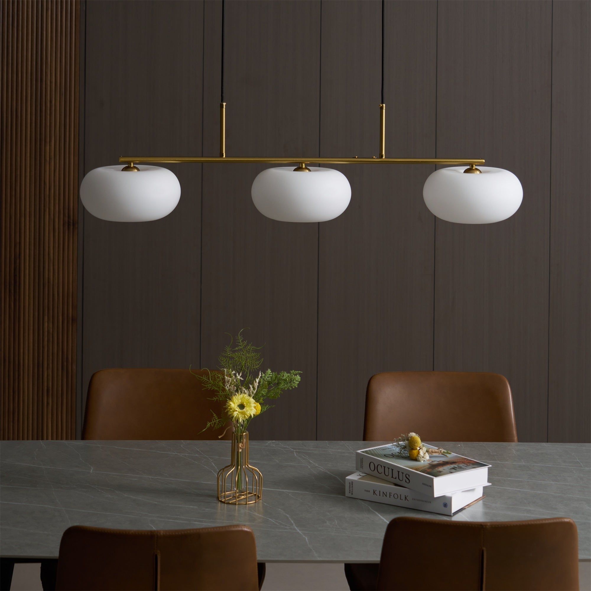 Unlit Clérachic gold-frame cream glass 3-light cluster over a marble table, dark wood panels and leather chairs.
