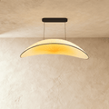 Clérachic cream pleated-fabric chandelier in a curved leaf shape, its shade glowing warm white below a black ceiling canopy.