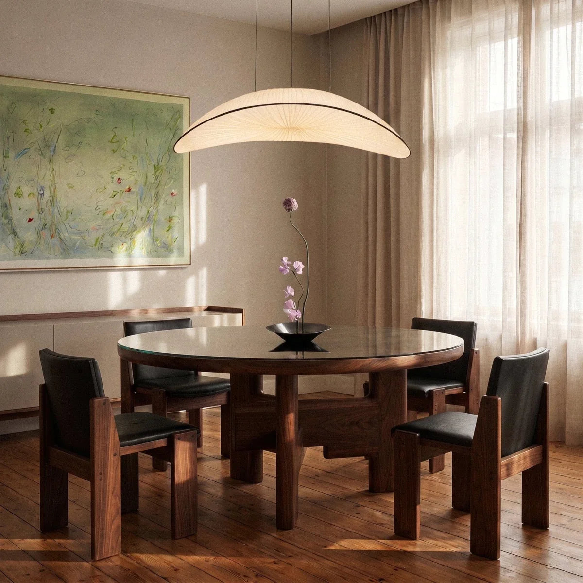 The Clérachic cream fabric chandelier glowing warm white above a round walnut dining table set with a single orchid stem.