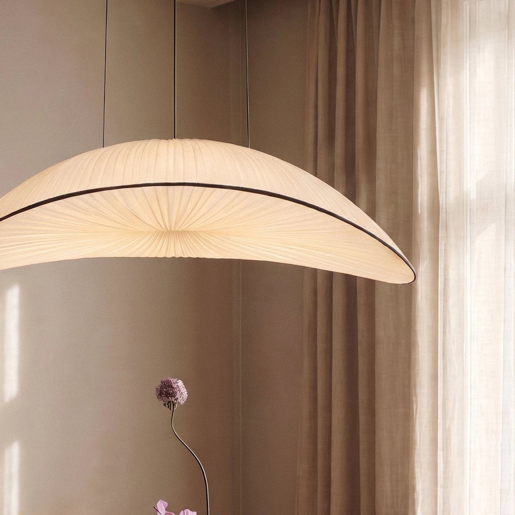 Close-up of the Clérachic cream fabric chandelier's pleated shade, glowing warm white beside a dried flower stem.