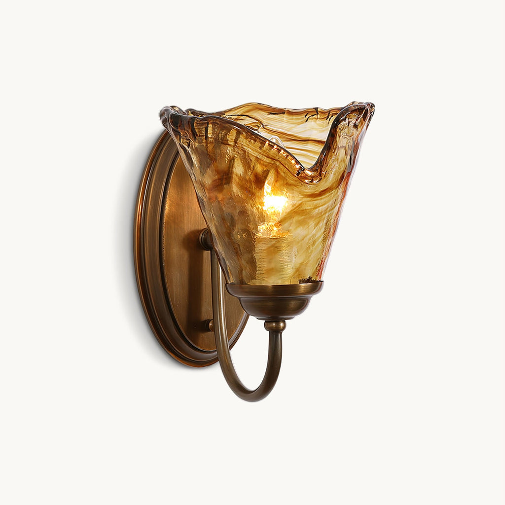 Crinkled amber glass shade with a flared edge on an oval antique brass backplate, on this Clérachic wall sconce, on white.