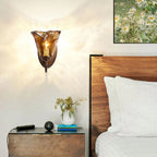 Above a wooden bedside table with a vase of dried stems, this Clérachic amber glass sconce hangs next to a walnut headboard.