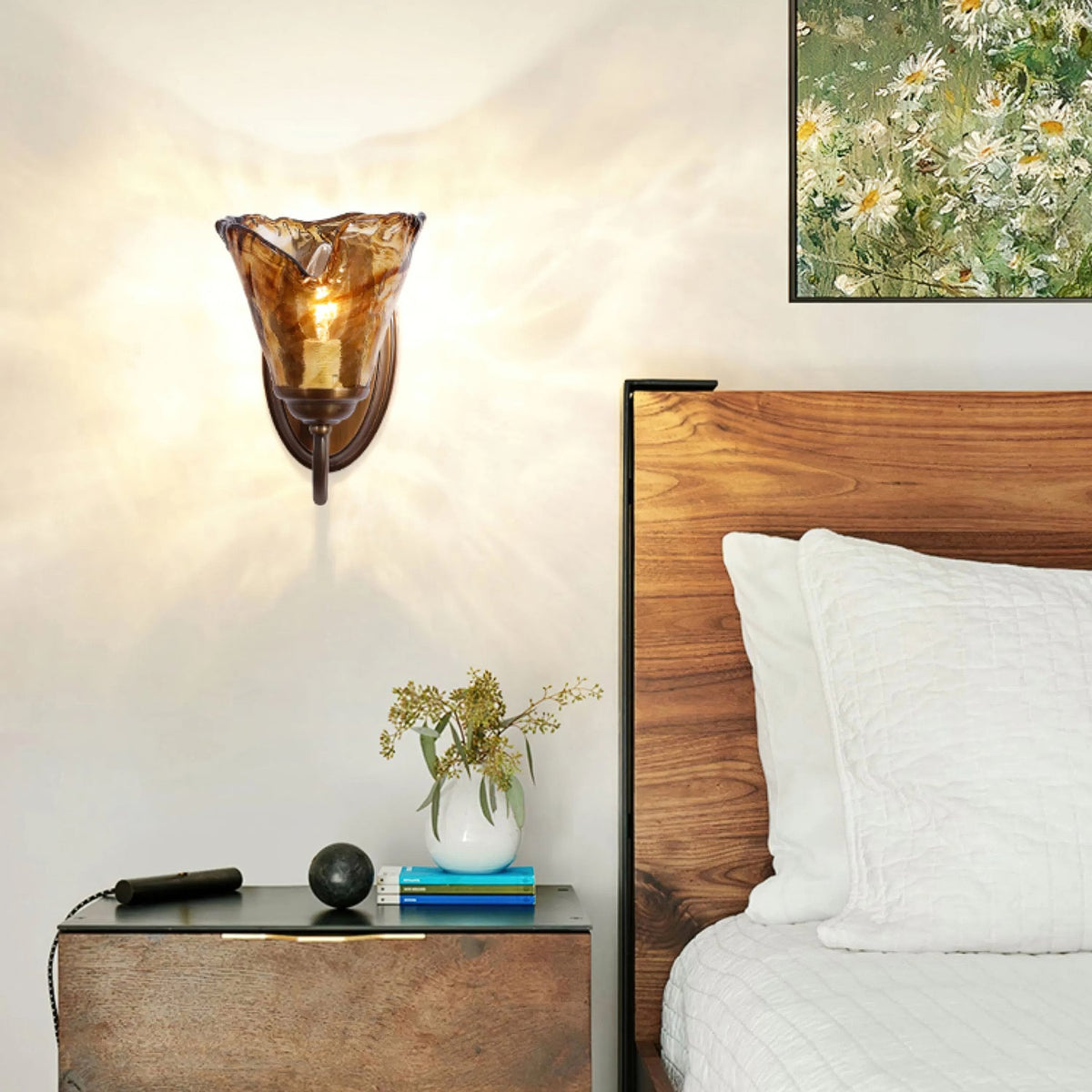 Above a wooden bedside table with a vase of dried stems, this Clérachic amber glass sconce hangs next to a walnut headboard.