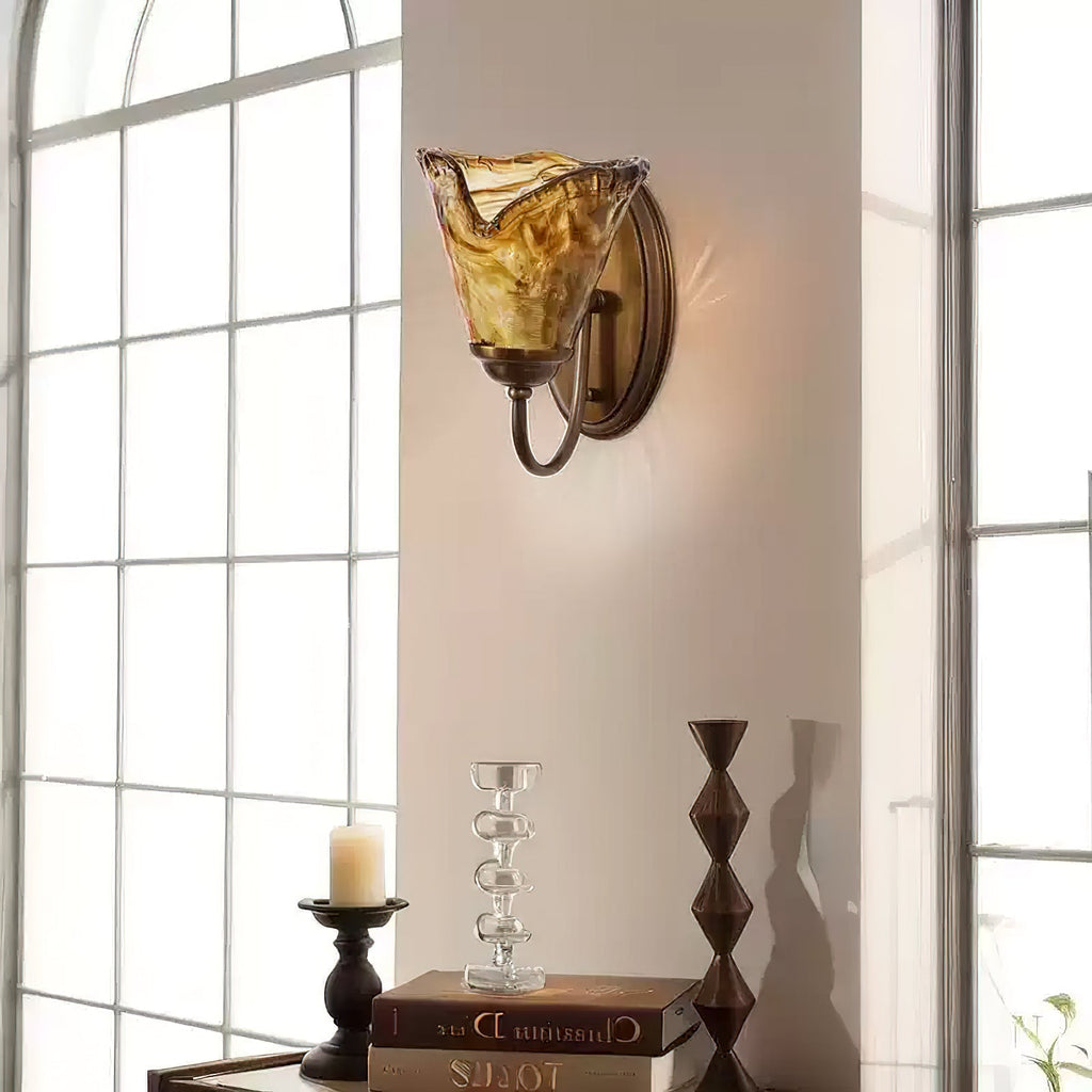 Next to a tall paned window, a Clérachic sconce in crinkled amber glass glows above a candlestick and a stack of books.