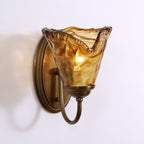 Three-quarter view of the swirled amber and brown glass shade on this Clérachic wall sconce, with its antique brass arm and backplate.