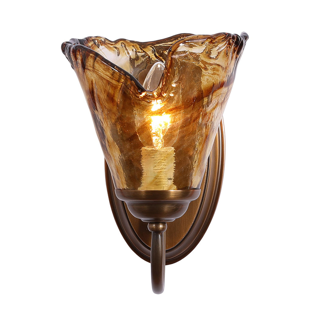 Straight-on view of this Clérachic wall sconce, its amber glass shade lit around a candle-style bulb, on an oval brass backplate.