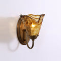 Seen from the side, the oval antique brass backplate and curved arm hold the lit amber shade of this Clérachic wall sconce.