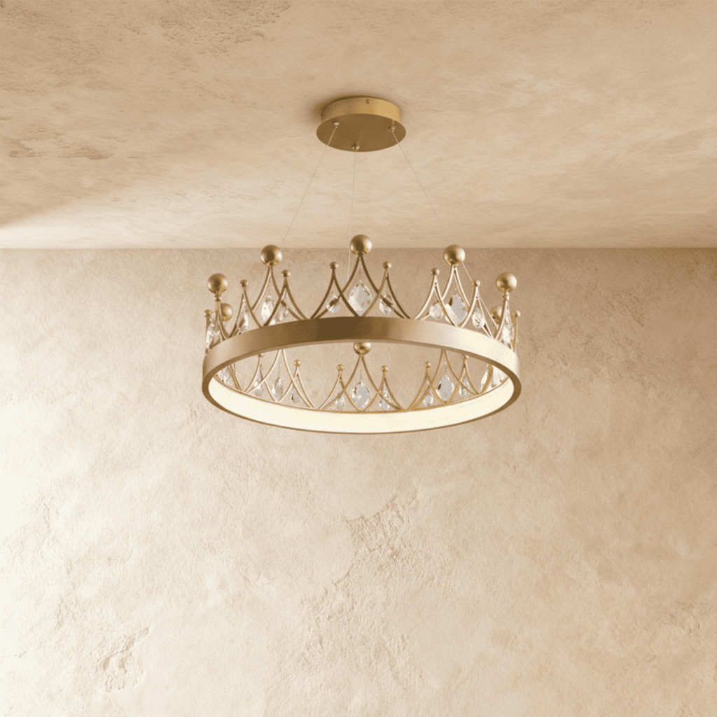 Clérachic crown-shaped gold ring chandelier with kite-cut crystals and gold ball finials, lit from below against a limewash wall.