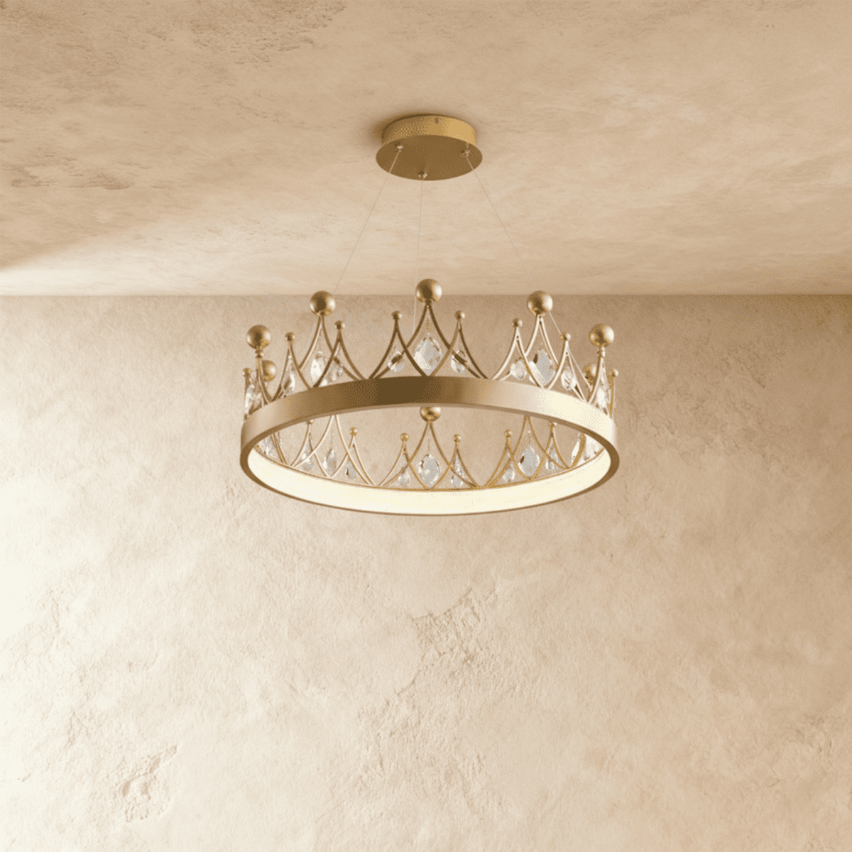 Clérachic crown-shaped gold ring chandelier with kite-cut crystals and gold ball finials, lit from below against a limewash wall.
