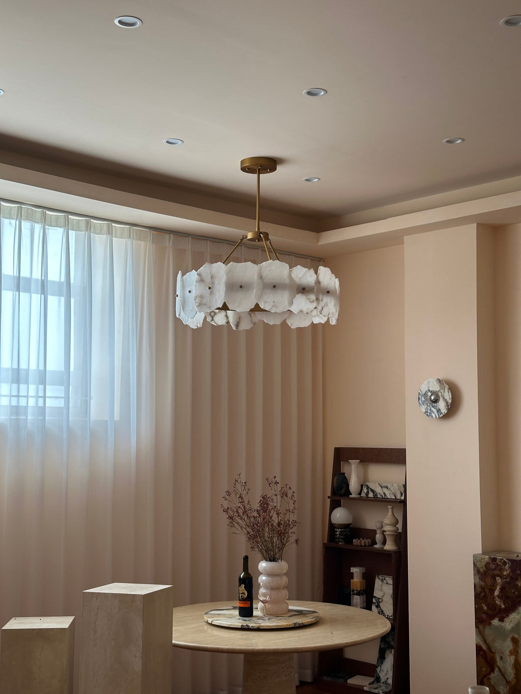 The Clérachic Cryon in a blush dining nook, hung over a travertine table beside sheer floor-length curtains.