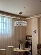 The Clérachic Cryon in a blush dining nook, hung over a travertine table beside sheer floor-length curtains.