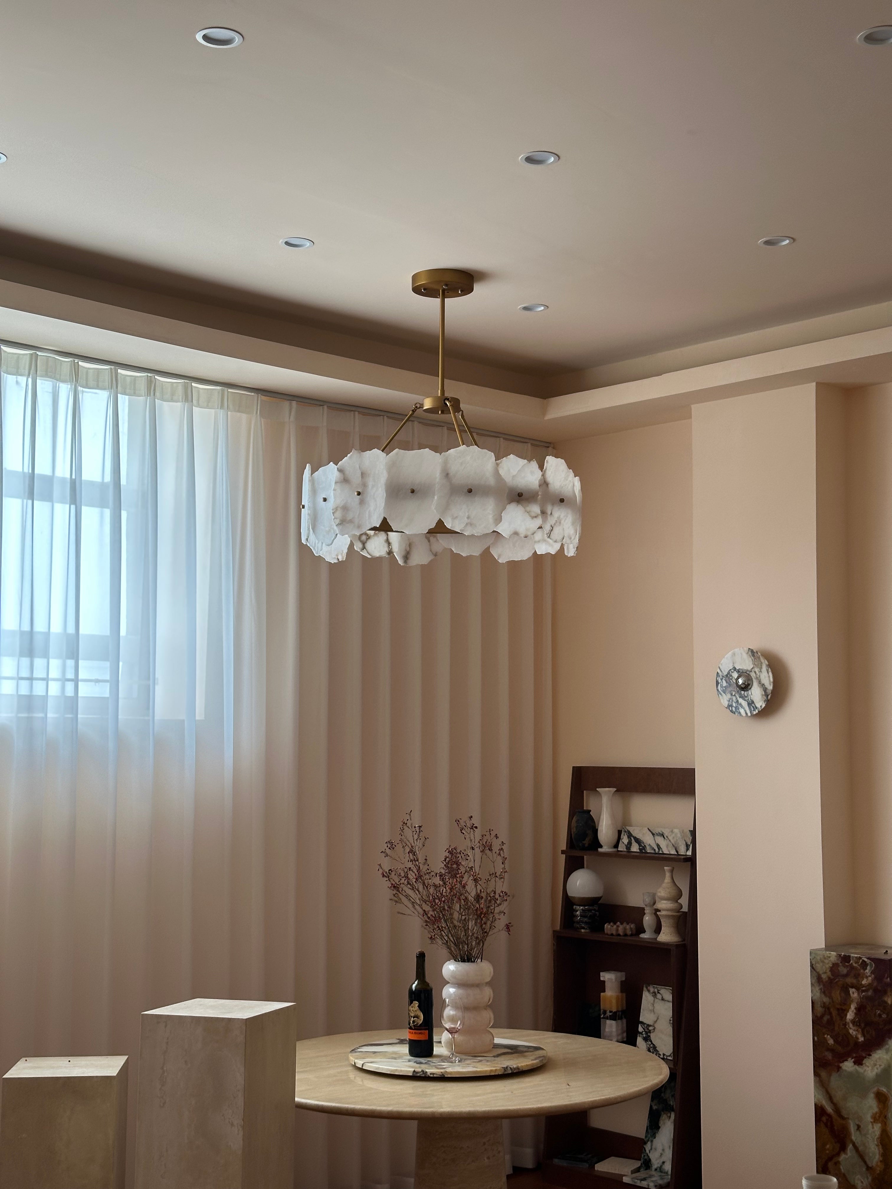 The Clérachic Cryon in a blush dining nook, hung over a travertine table beside sheer floor-length curtains.