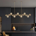 This Clérachic chandelier hangs from two thin rods in a dark fluted kitchen, its crystal balls glowing above a bar with a tan stool.