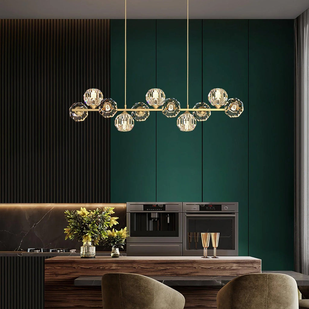 A long brass bar of crystal balls over a walnut kitchen island, a Clérachic chandelier set against deep green cabinets.