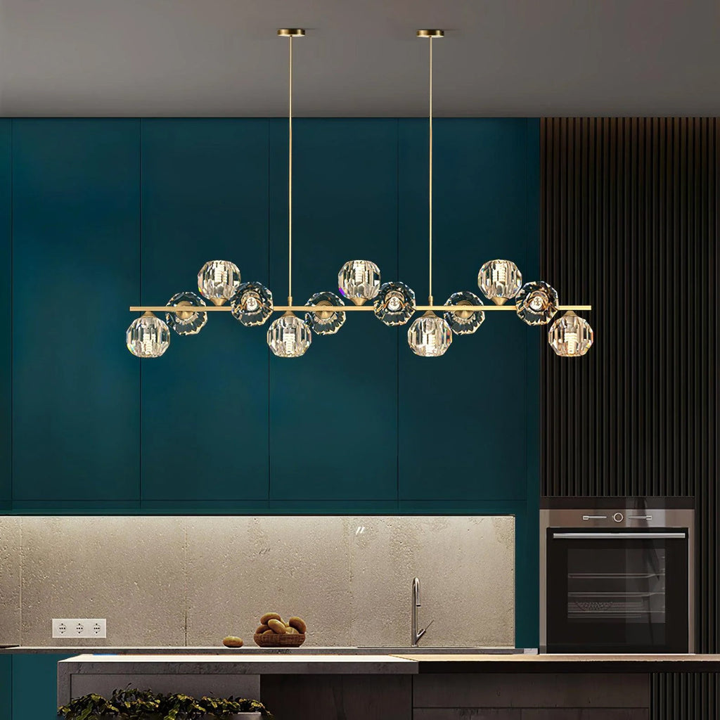 Brass bar and crystal balls hanging in front of green cabinets with a built-in oven, a Clérachic chandelier in a kitchen.