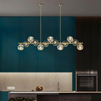 Brass bar and crystal balls hanging in front of green cabinets with a built-in oven, a Clérachic chandelier in a kitchen.