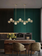 Seen narrower in a green-panelled dining room, a Clérachic crystal chandelier hangs over a wooden table and two olive chairs.