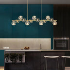 Crystal balls glow along the brass bar in a teal kitchen with stone backsplash and pale stools, a Clérachic chandelier.