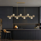 A rectangular canopy holds this Clérachic chandelier over a dark fluted kitchen island, brass bar and crystal balls lit.