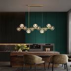 Over a wooden dining island with two olive armchairs, this Clérachic chandelier sits against green and dark panelling.