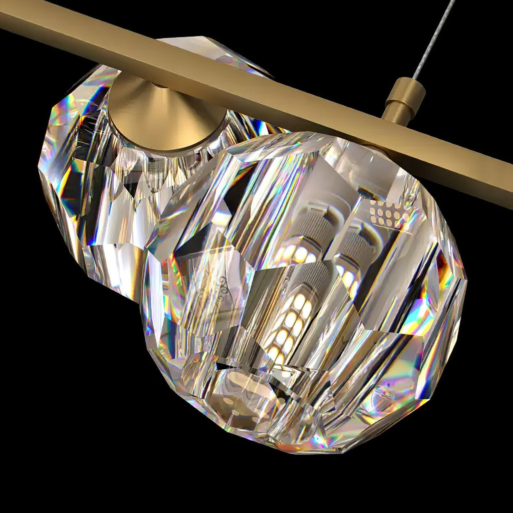 Close view of two faceted crystal balls and the flat brass bar on this Clérachic chandelier, a light bulb glowing inside.