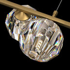Close view of two faceted crystal balls and the flat brass bar on this Clérachic chandelier, a light bulb glowing inside.