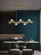 A Clérachic chandelier hangs above a slim white desk in a dark panelled study with teal doors and grey stools.