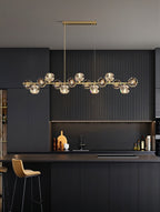 Tall view of a Clérachic chandelier in a dark kitchen, the crystal balls evenly spaced along a brass bar above the island.