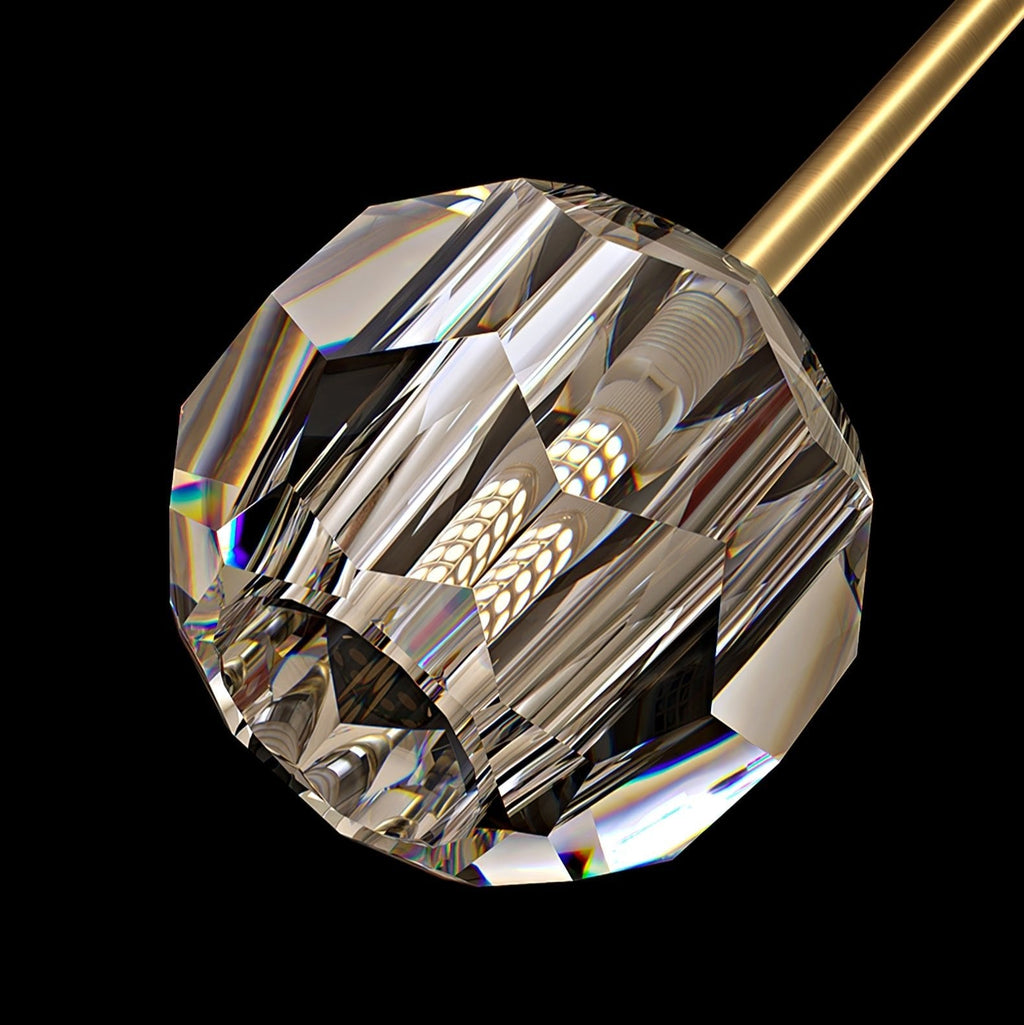 Close view of one faceted crystal ball with a bulb inside, hanging from the brass bar of this Clérachic chandelier.