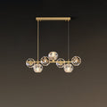 Seven crystal balls on a short brass bar, this Clérachic chandelier hanging from a rectangular canopy on a brown wall.