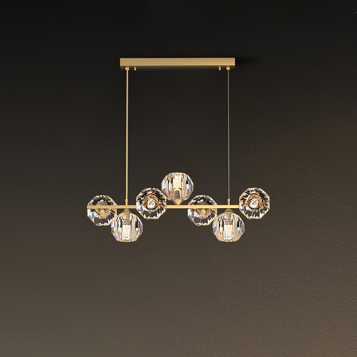 Seven crystal balls on a short brass bar, this Clérachic chandelier hanging from a rectangular canopy on a brown wall.